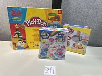 Front view of three boxed sets: Play-Doh Advent Calendar, Cra-Z-Art Softee Dough Fancy Tea Party, Play-Doh Kitchen Creations skillet set