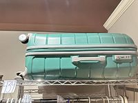 Full view of teal Samsonite suitcase on shelf showing wheel, size and shell condition