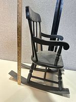 Left side view of black painted child's rocking chair showing ruler for scale