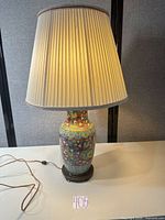 Full view of lamp illuminated showing porcelain body, shade, cord and base