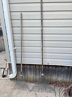 Two full-length metal leaf rakes leaning against siding