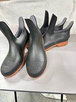 Two pairs of black ankle rain boots standing on table