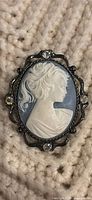 Front view of blue and white cameo brooch pendant showing female profile and rhinestone-accented frame