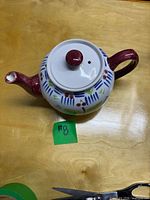 Top view of ceramic teapot showing burgundy spout and handle, white lid with burgundy knob and vent hole, patterned body