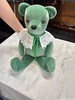 Front view of green velvet teddy bear seated on table