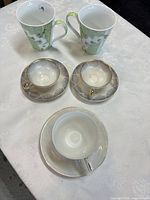 Two green orchid mugs, three saucers, one cup on saucer displayed on table