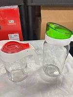 Both clear glass pitchers side by side showing colored lids, white handles, overall design and relative sizes