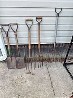 five yard tools lined against wall: two spades, two garden forks, one wide pitchfork