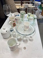 Overall lot on table showing glass goblets, mugs, sugar bowl, plates and small cups