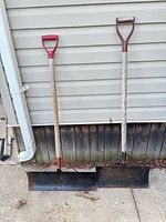 Pair of 24" steel scrapers leaning on siding showing full length and blade width