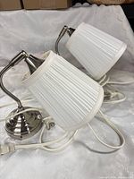 pair of chrome wall lamps with white pleated shades, cords visible