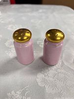 Front view of both pink porcelain shakers showing gold tops