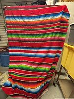 Full view of large red serape blanket hanging to show overall size, colour and stripe pattern