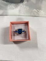 Ring in box with blue center stone and side accents visible