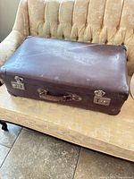 Closed brown hard-sided suitcase on couch, showing exterior wear and hardware