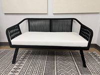 Full front view of black metal and cord patio bench with white cushion