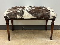 Full front view of bench showing cowhide seat and reeded legs