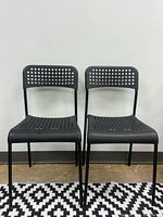 Front view of the pair of black perforated plastic chairs