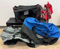 Three duffel bags stacked on bench with folded red camping chair