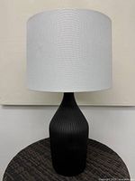 Full view of lamp showing black ribbed base and white drum shade