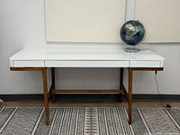 Front view of desk showing white laminate top, wood base, globe for scale