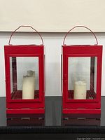 Front view of two red metal lanterns with candles inside