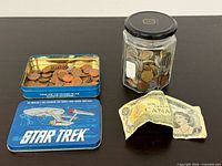 Jar of coins, open Star Trek tin with coins, two Canadian $1 banknotes
