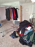 Clothing rack with hanging jackets and pile of assorted garments on floor