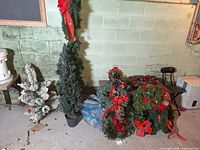 Group showing two slim green trees, white flocked tree, pile of wreaths and garland