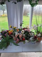 Table with multiple artificial floral arrangements in various pots and vases