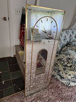 Front view showing full mirrored surface, gold frame, dial and pendulum window