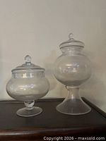 Both glass apothecary jars with lids shown side by side