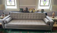 Front view of the gray tufted sofa showing full length, back, seat, legs, and bolsters
