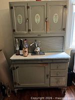 Front view of gray Hoosier style cabinet closed showing three upper doors, tambour center, enamel counter, lower door and drawers