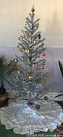 Assembled silver tinsel tree standing on floor with skirt (skirt and ornaments excluded)