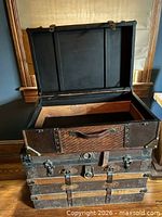 Steamer trunk open showing interior wood, metal hinges, woven panel accent on exterior front