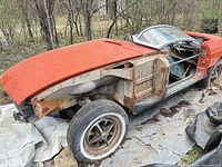 Passenger side view of largely stripped red MG MGB shell with missing front fender and wheel removed