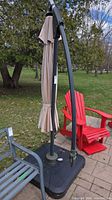Closed beige cantilever umbrella on black fillable base beside patio chairs