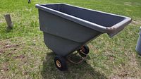 Side view of gray plastic two-wheel dump cart on grass