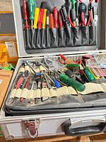 Open aluminum case showing screwdrivers, pliers, picks, files and goggles