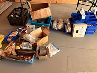 Overview of assorted containers including blue parts bins, cardboard boxes, milk crate and contents
