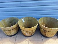 three wooden half-barrel planters side by side showing overall size, weathering and plastic liners inside