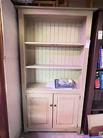 Front view of beige solid wood bookcase with two shelves and lower cabinet
