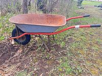 Side view of steel wheelbarrow showing rusted tray, red handles, single pneumatic tire