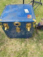 Front view of blue cube trunk showing brass-tone latches, lock and corner hardware
