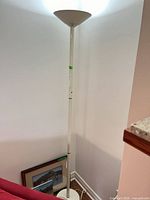 Full view of white torchiere floor lamp showing pole, base and illuminated shade