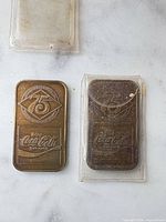 Front view of both commemorative bars showing 75 logo and Coca-Cola script