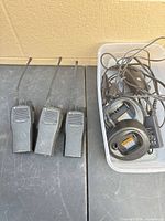 Three Motorola CP200 radios alongside bin containing chargers and adapters