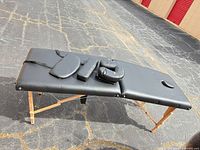 Full view of folded-out black vinyl massage table with accessories placed on top