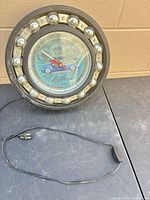 Front view of round automotive themed wall clock with power cord visible